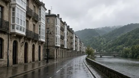Calle junto a la ría con edificios de piedra y miradores blancos bajo la lluvia en Bilbao